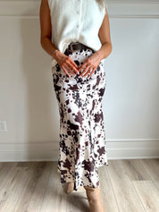 Woman wearing satin cow print maxi skirt with belt detail and white sweater top.