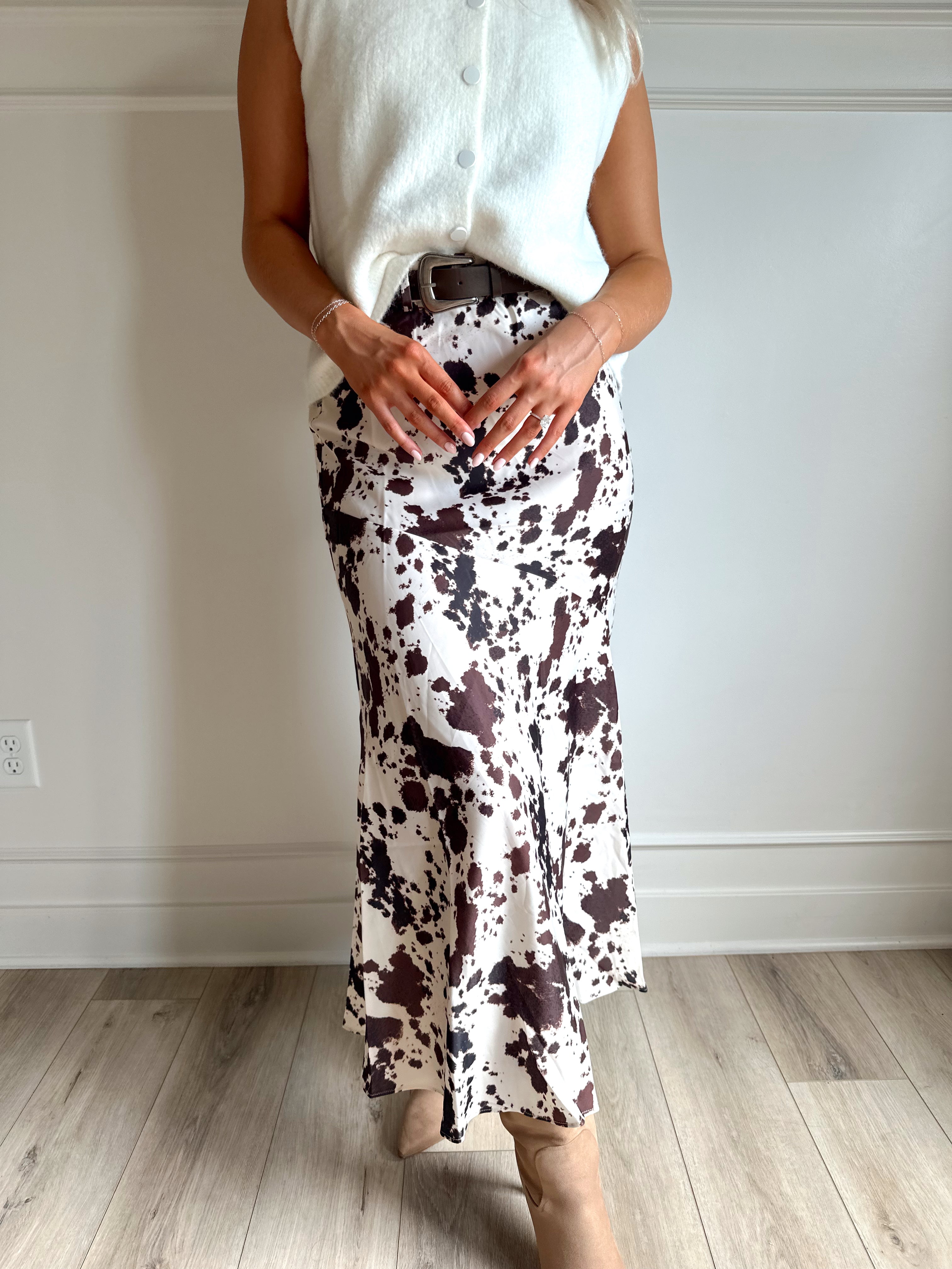 Woman wearing satin cow print maxi skirt with belt detail and white sweater top.