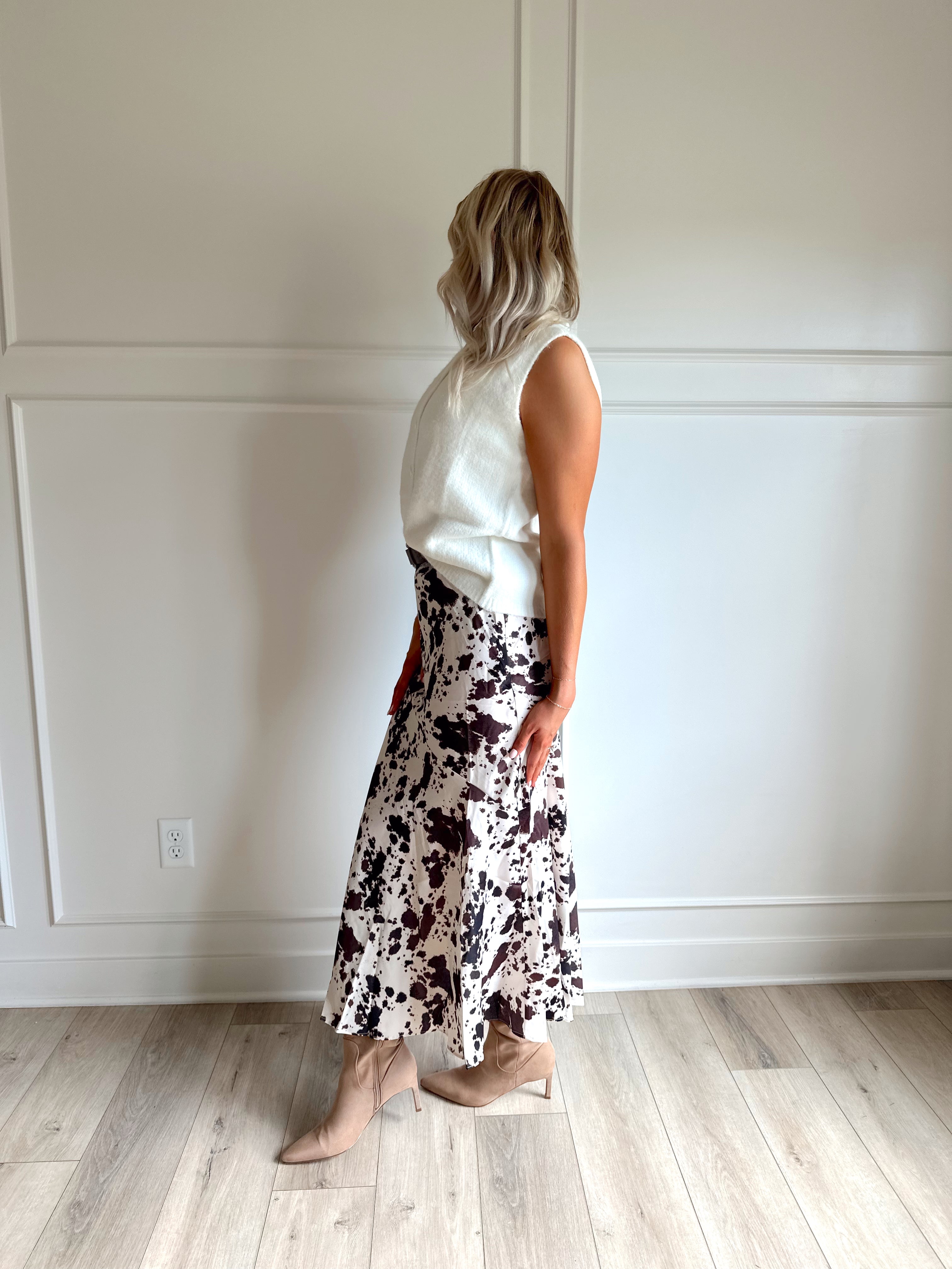 Woman wearing satin cow print maxi skirt with belt detail and white sweater top.