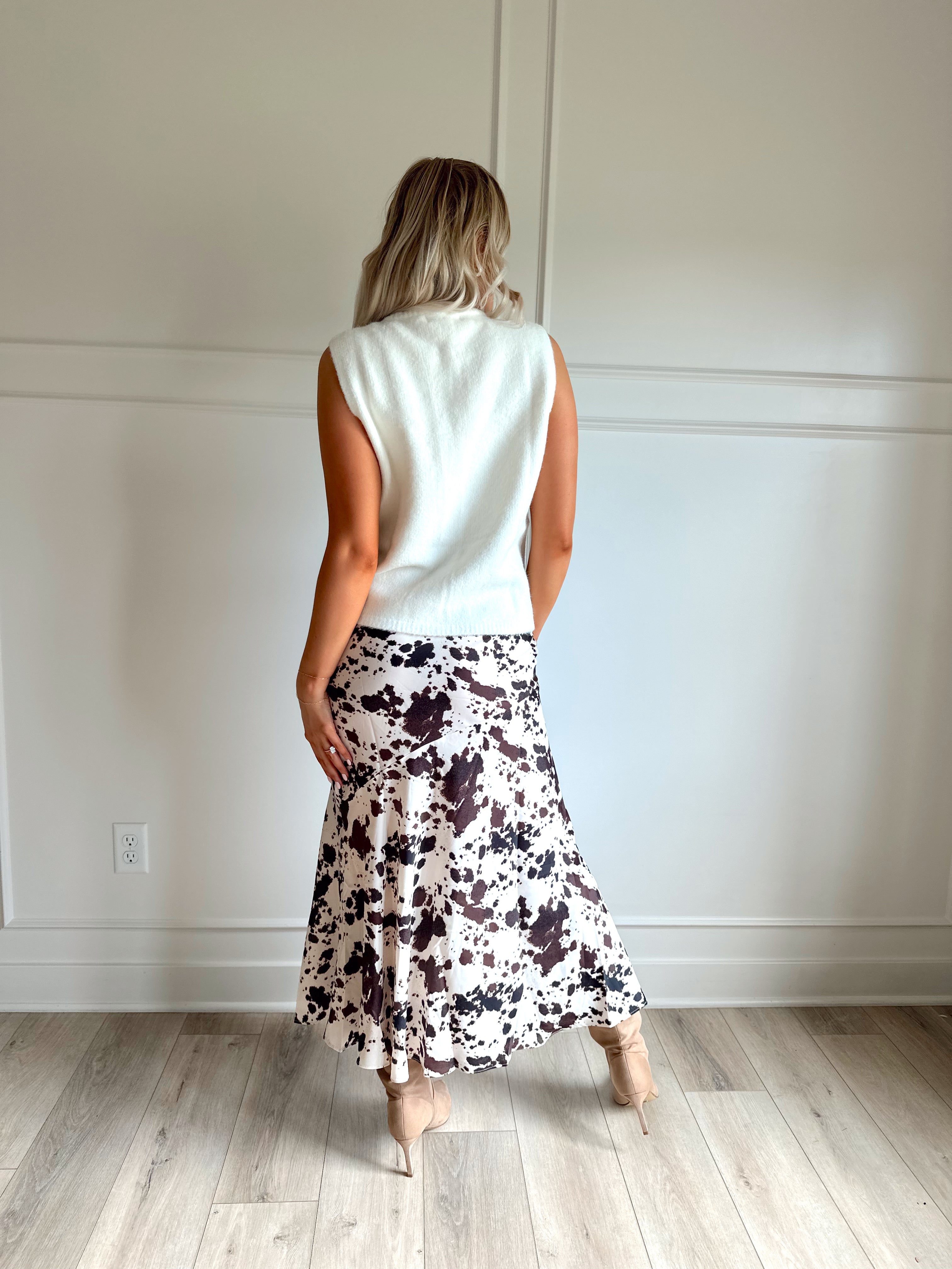 Woman wearing satin cow print maxi skirt with belt detail and white sweater top.