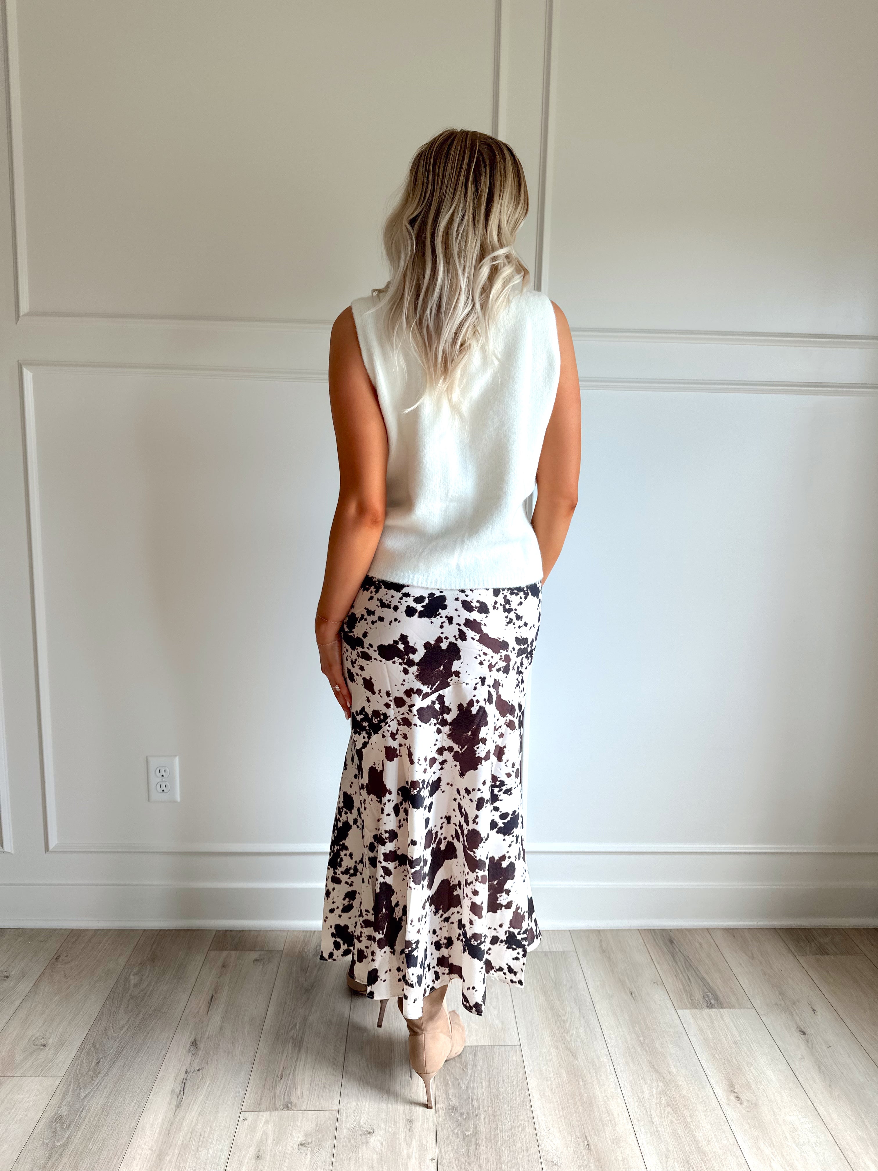 Woman wearing satin cow print maxi skirt with belt detail and white sweater top.