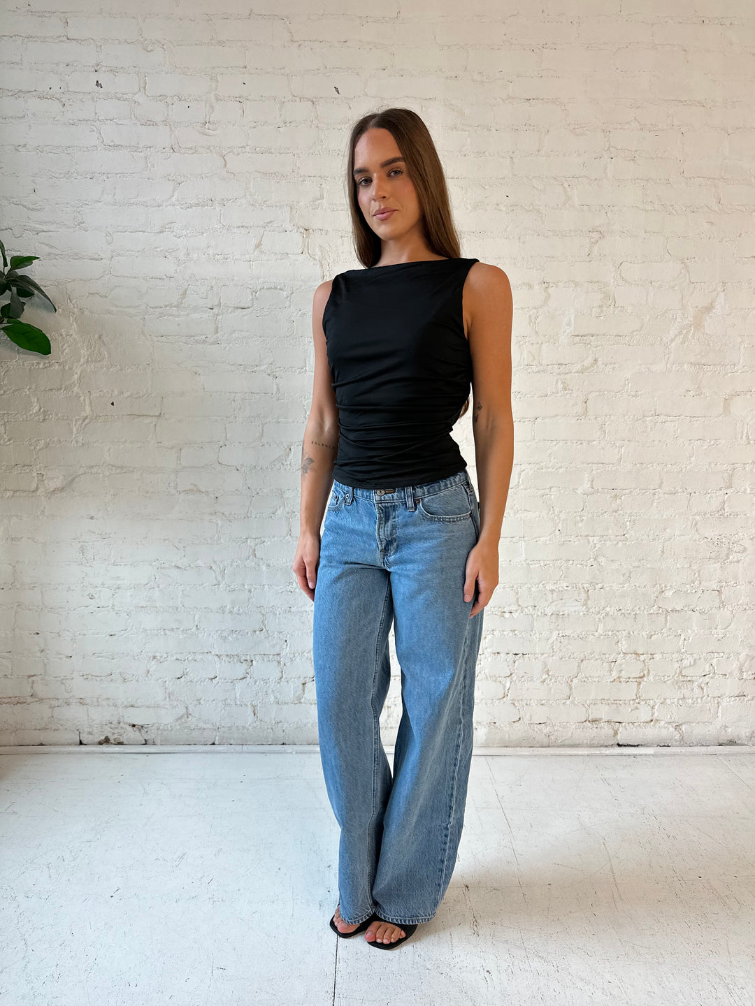 Woman wearing black ruched cowl neck top with open back and support strap.