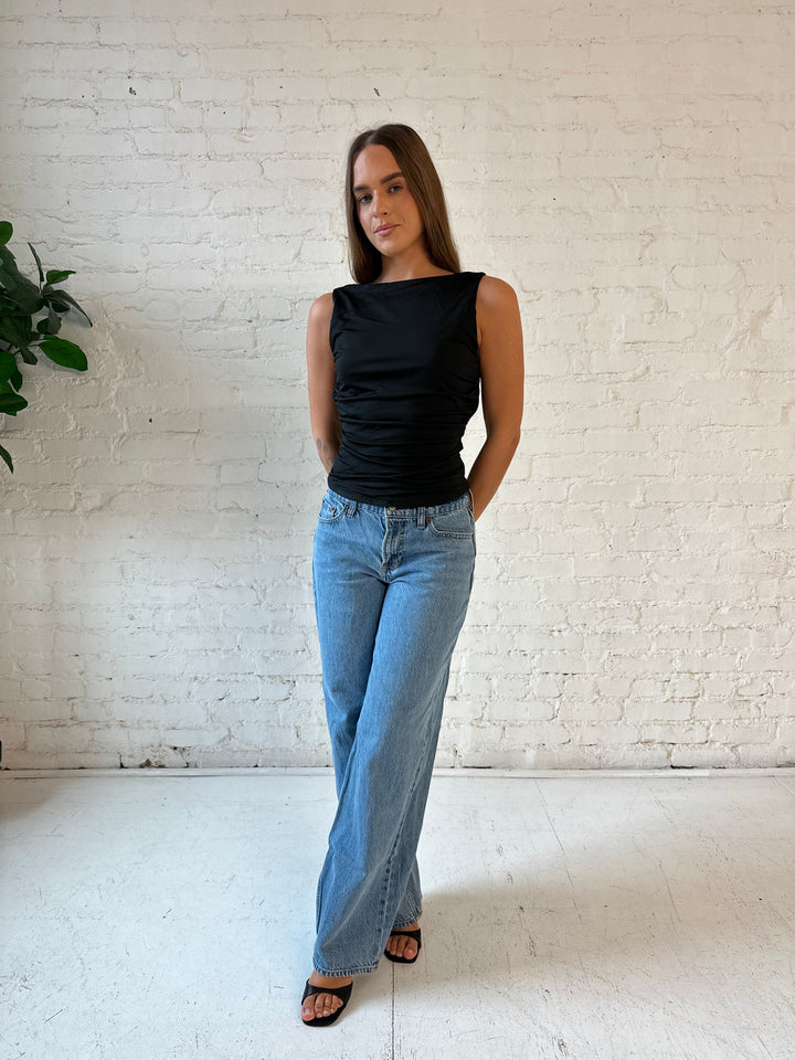 Woman wearing black ruched cowl neck top with open back and support strap.