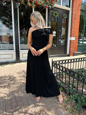 Woman wearing a black one shoulder maxi dress with flowy bottom.