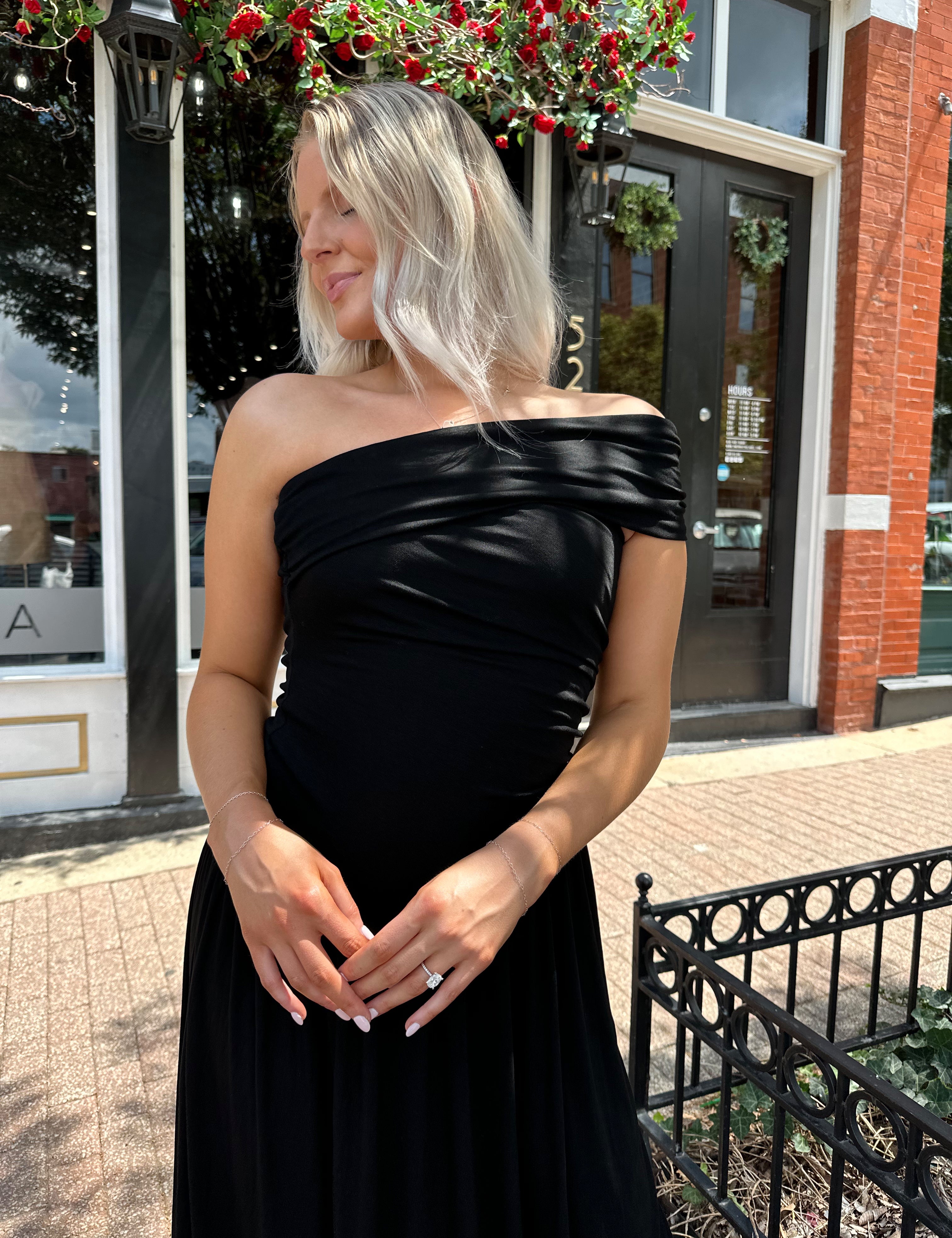 Woman wearing a black one shoulder maxi dress with flowy bottom.