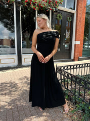 Woman wearing a black one shoulder maxi dress with flowy bottom.