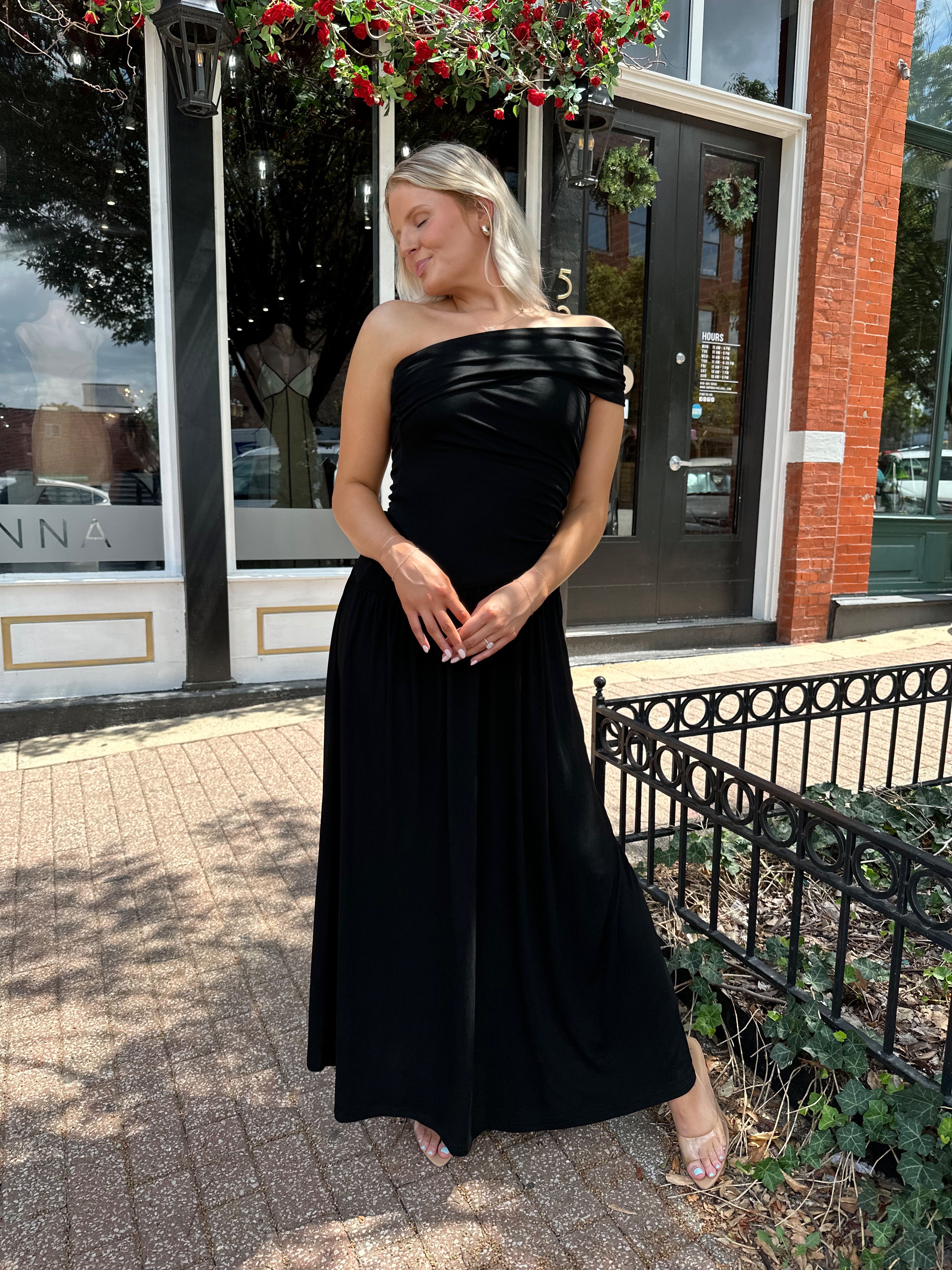 Woman wearing a black one shoulder maxi dress with flowy bottom.
