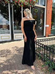 Woman wearing a black one shoulder maxi dress with flowy bottom.