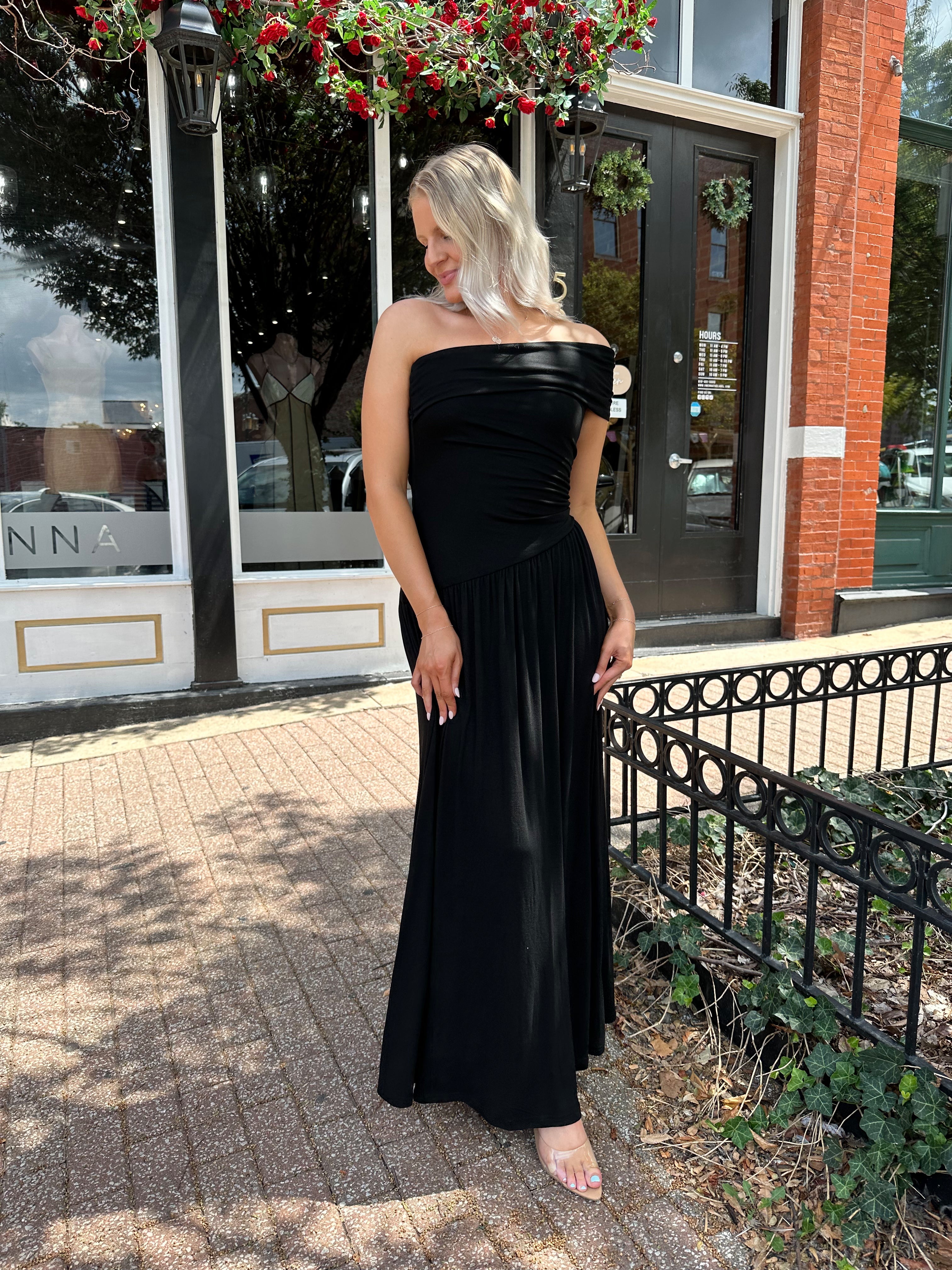Woman wearing a black one shoulder maxi dress with flowy bottom.