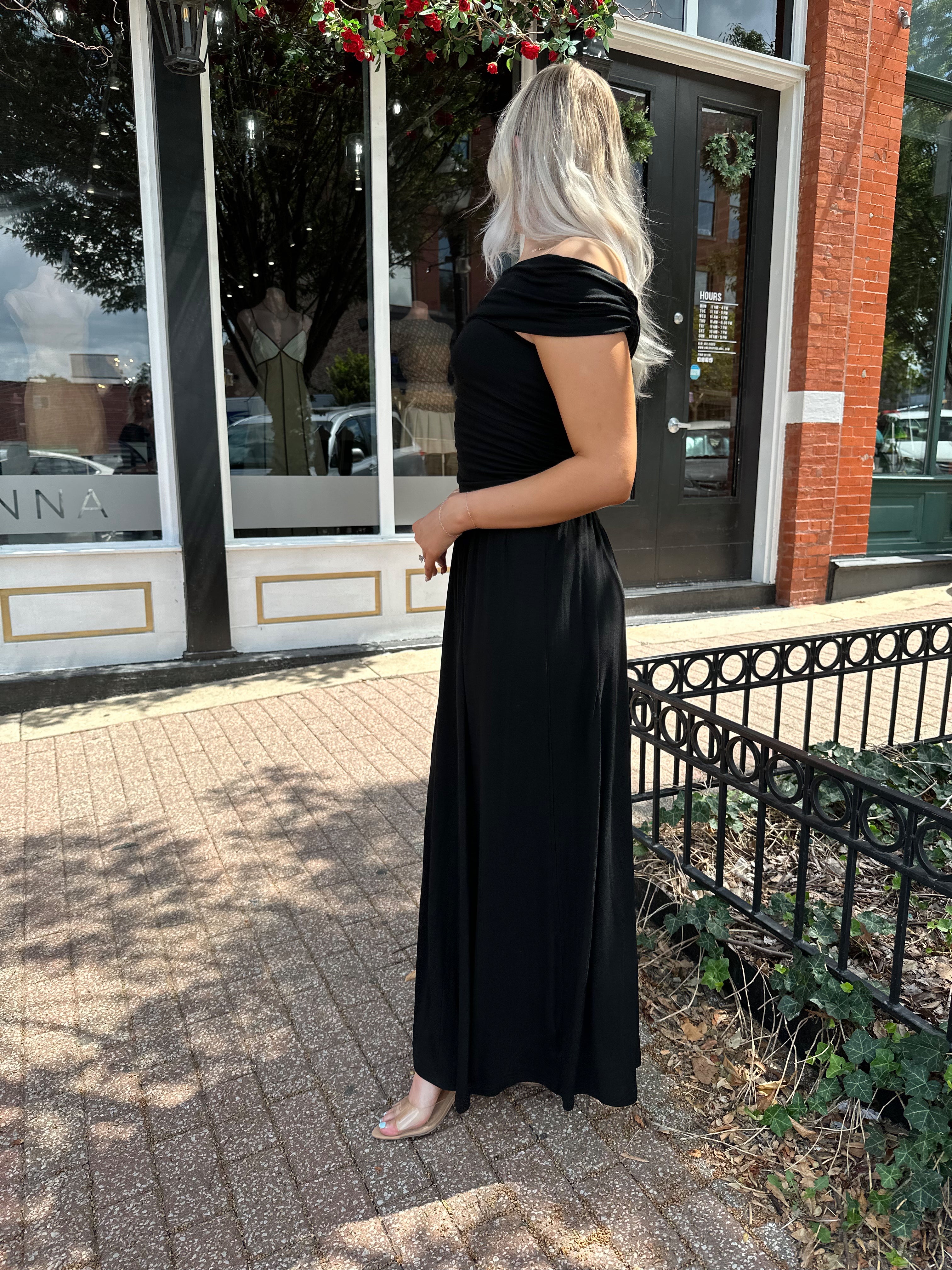 Woman wearing a black one shoulder maxi dress with flowy bottom.