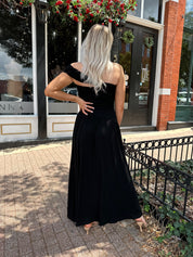Woman wearing a black one shoulder maxi dress with flowy bottom.