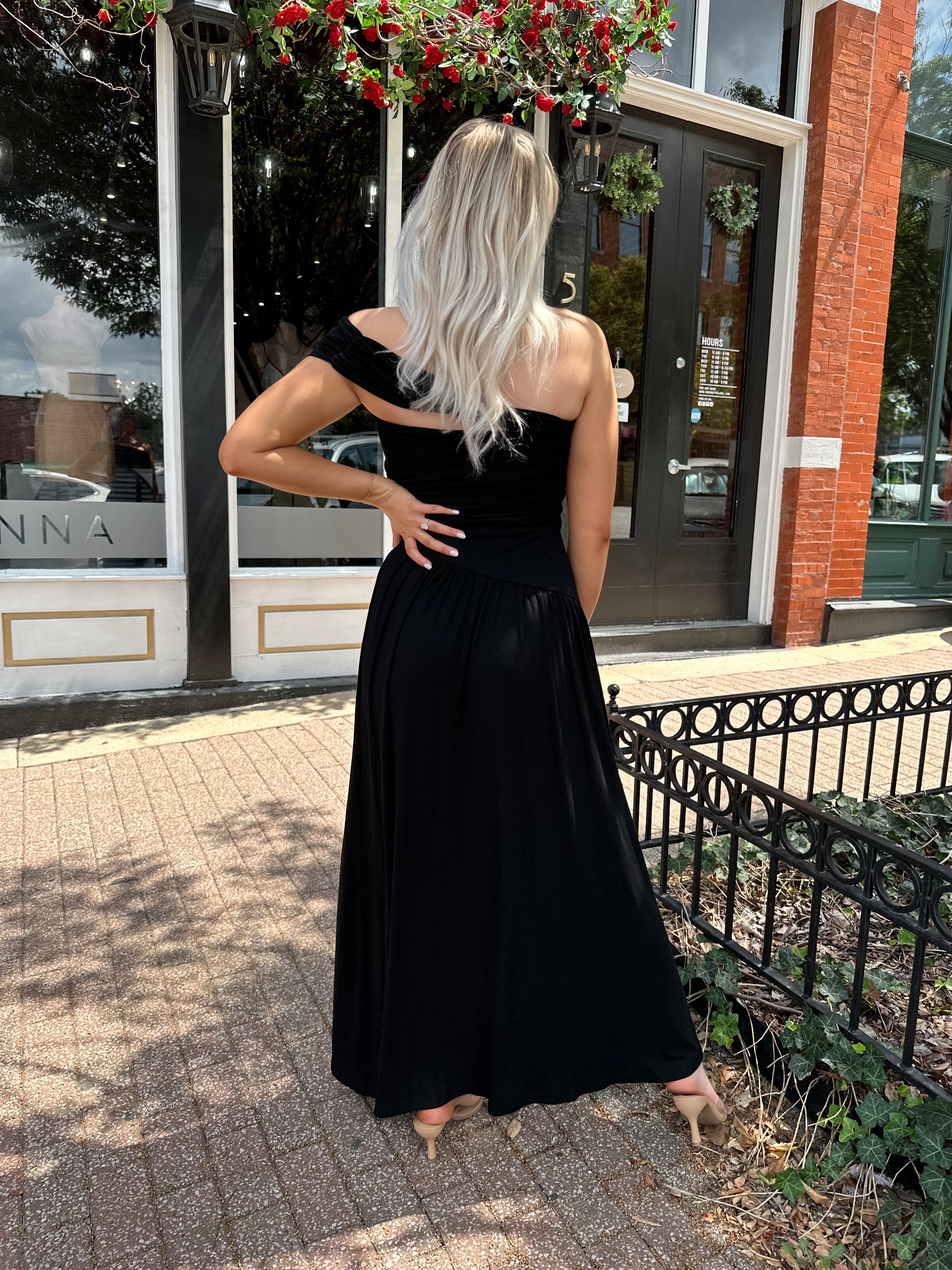 Woman wearing a black one shoulder maxi dress with flowy bottom.