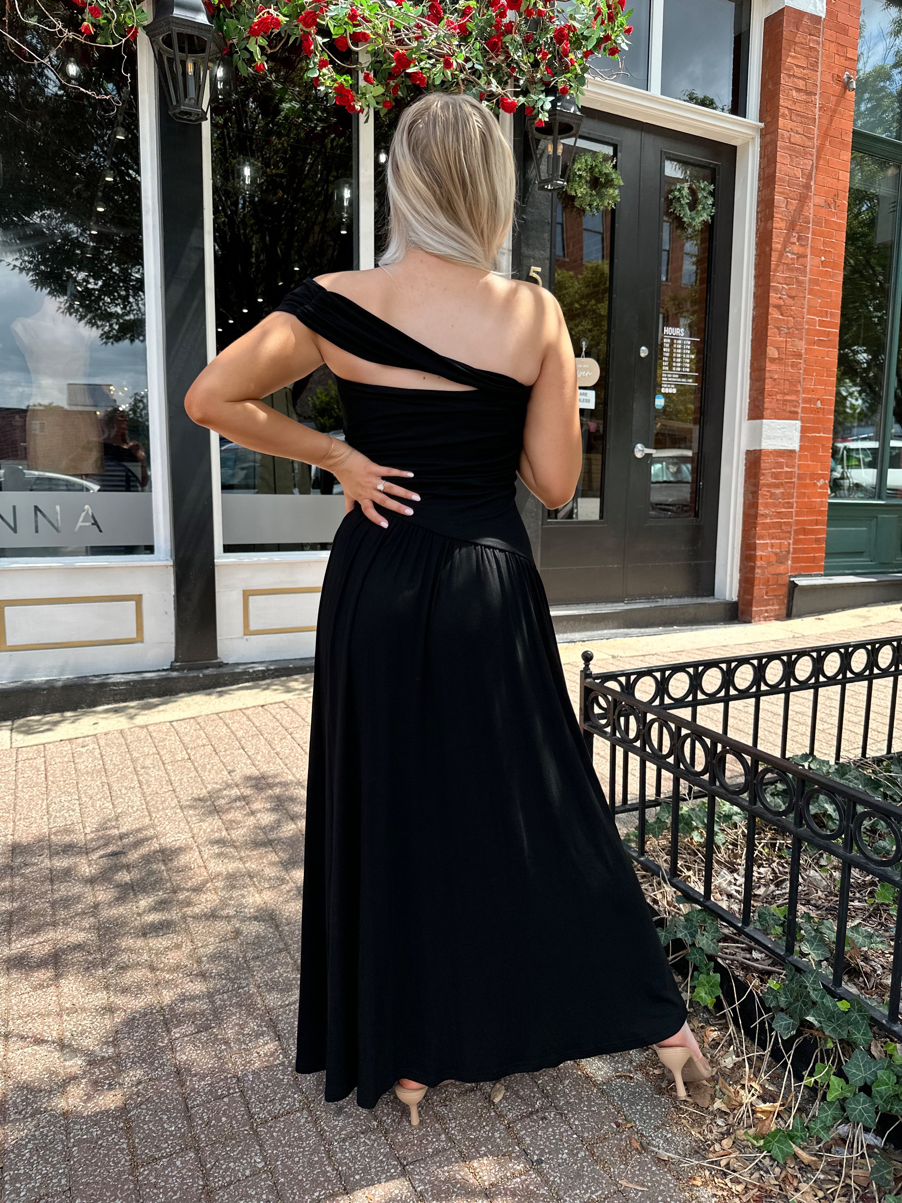 Woman wearing a black one shoulder maxi dress with flowy bottom.