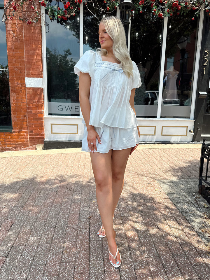 Woman wearing white two piece set with a puff sleeve babydoll top and flowy shorts. 