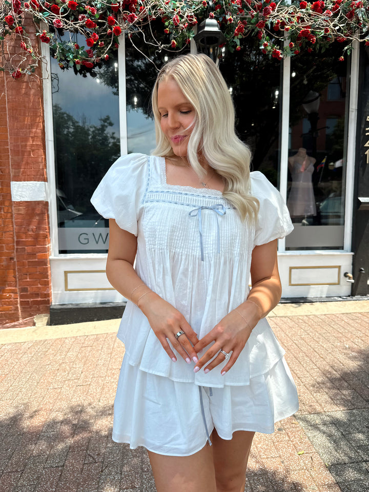 Woman wearing white two piece set with a puff sleeve babydoll top and flowy shorts. 