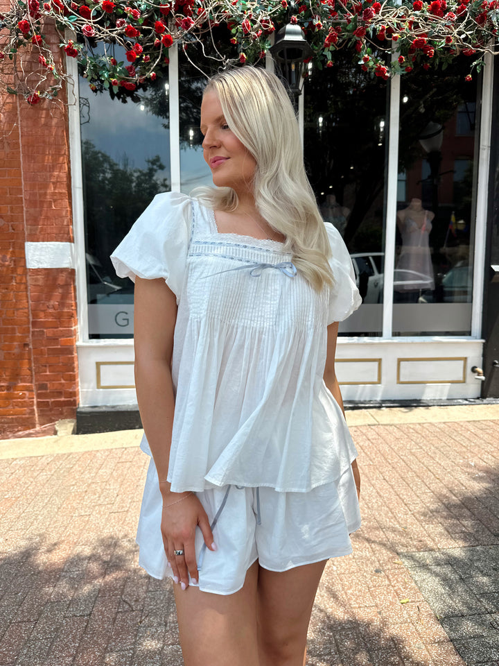 Woman wearing white two piece set with a puff sleeve babydoll top and flowy shorts. 
