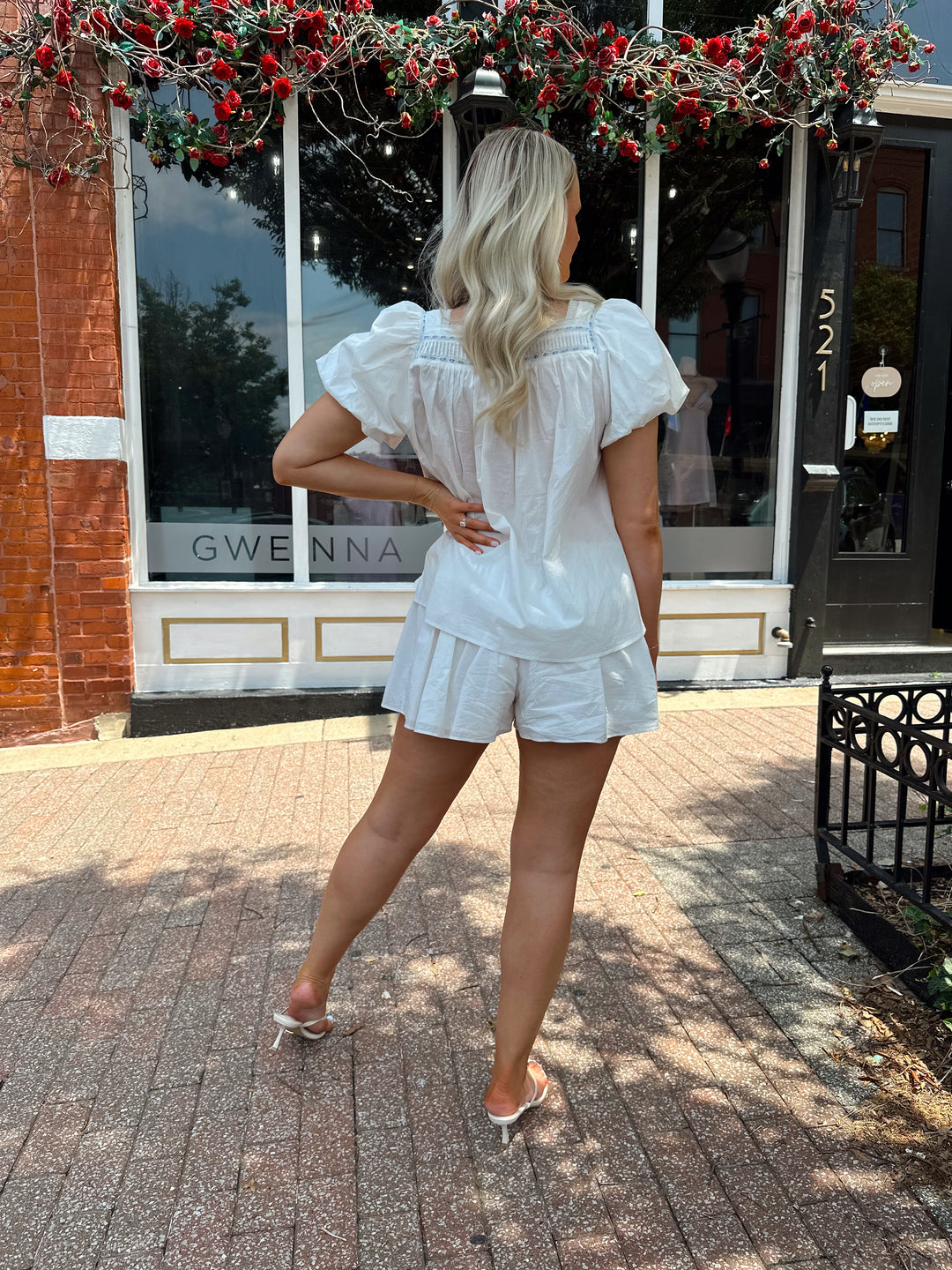 Woman wearing white two piece set with a puff sleeve babydoll top and flowy shorts. 