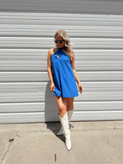 Model wearing blue halter neck mini dress with white boots on a sunny day