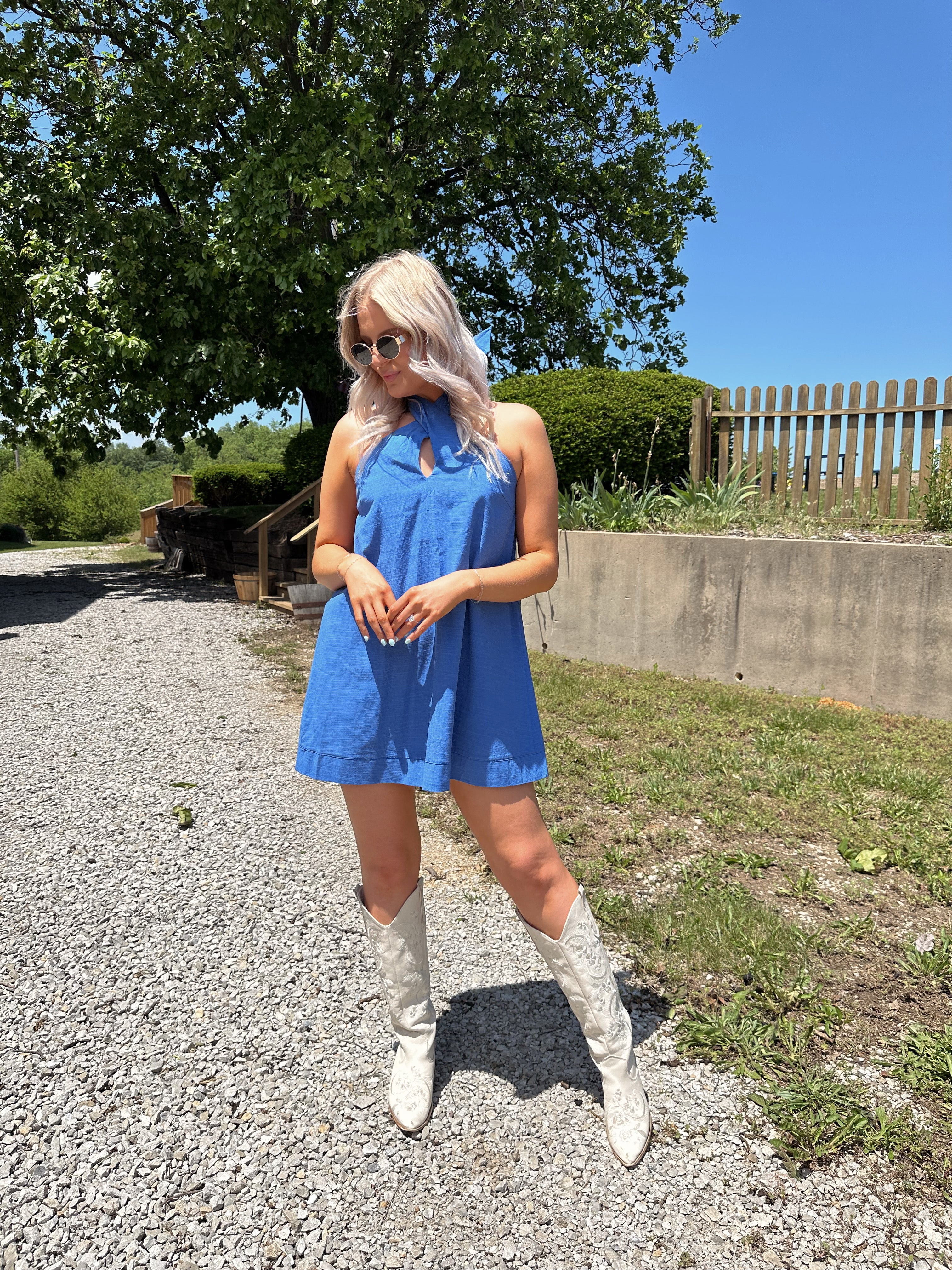 Model wearing blue halter neck mini dress with white boots on a sunny day