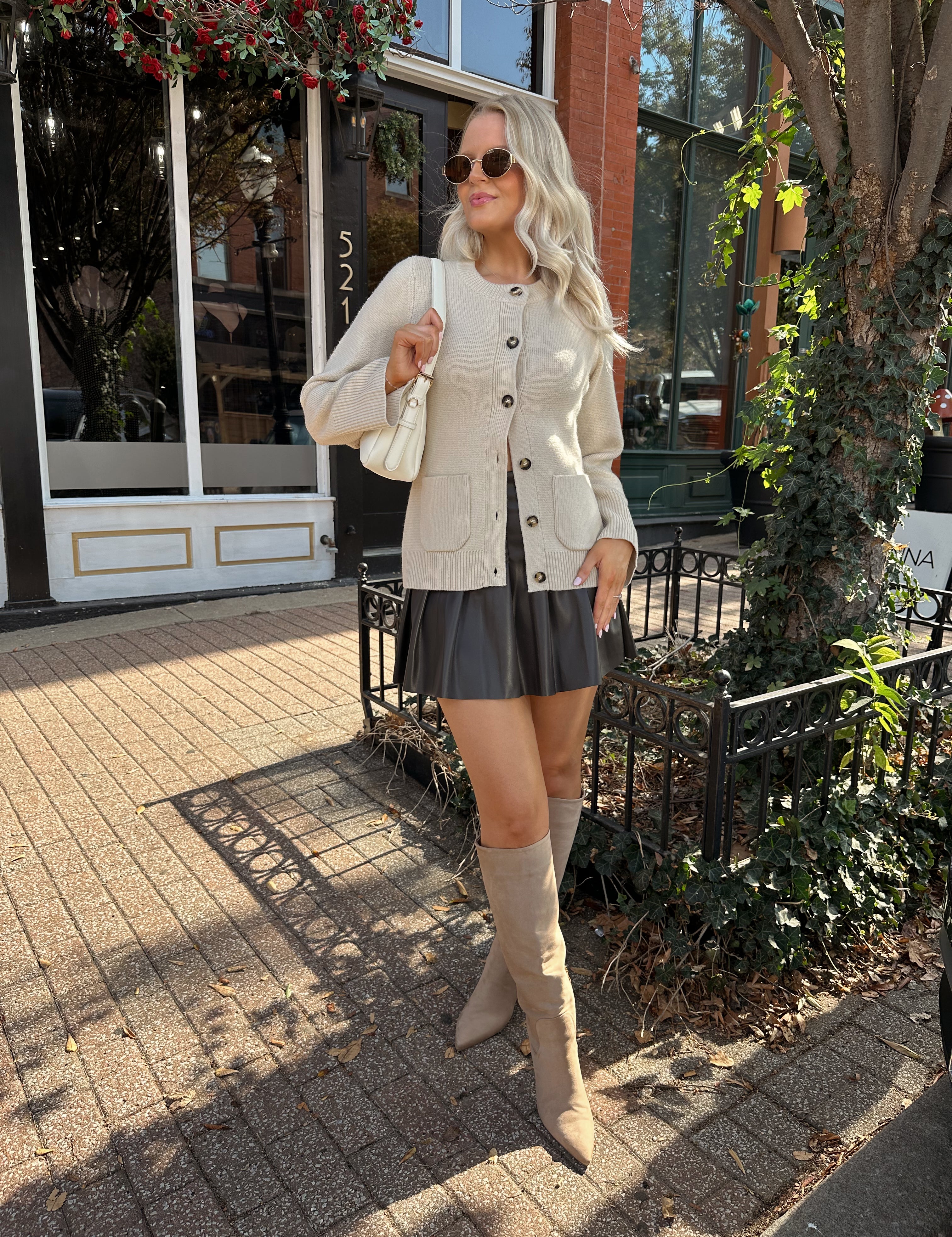 Woman wearing ecru button up fitted cardigan with brown leather mini skirt. 