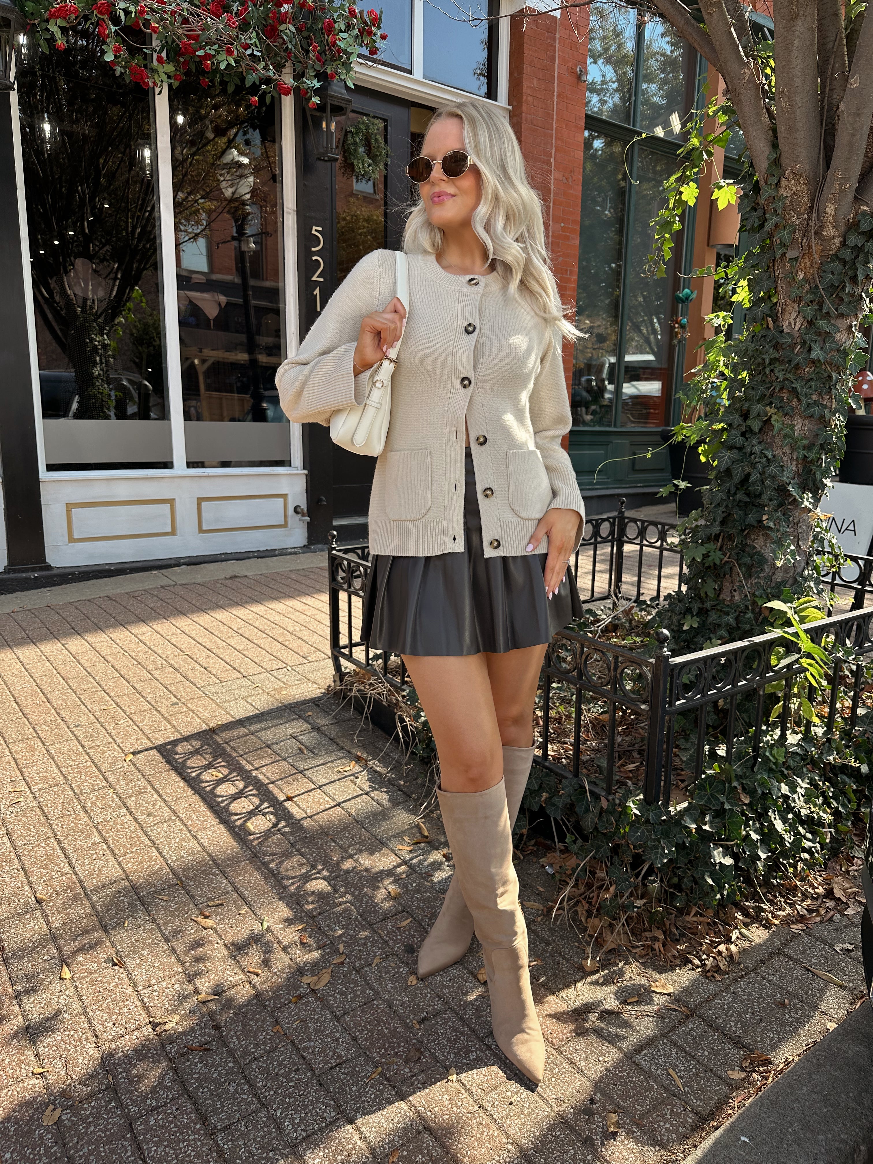 Woman wearing ecru button up fitted cardigan with brown leather mini skirt. 