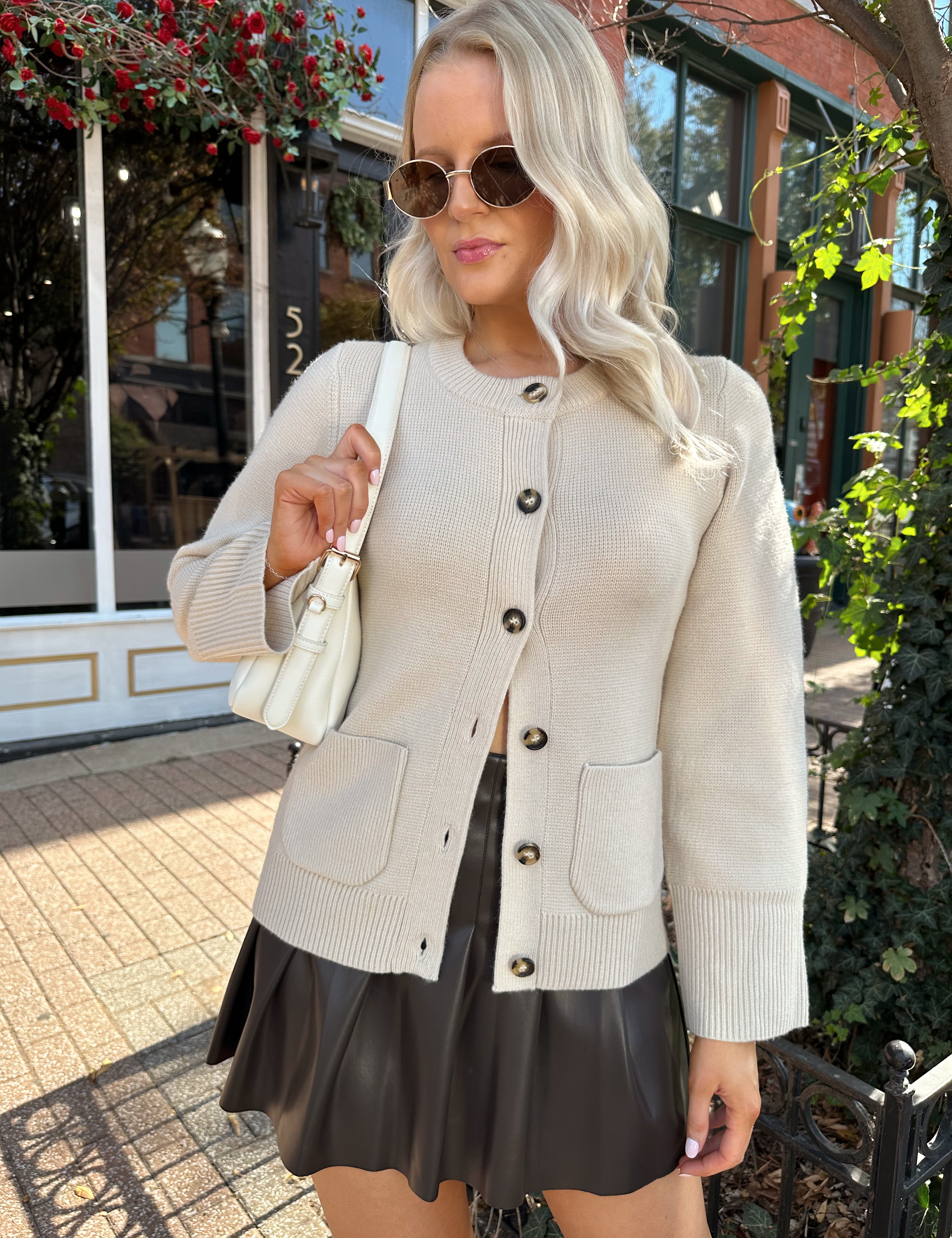 Woman wearing ecru button up fitted cardigan with brown leather mini skirt. 