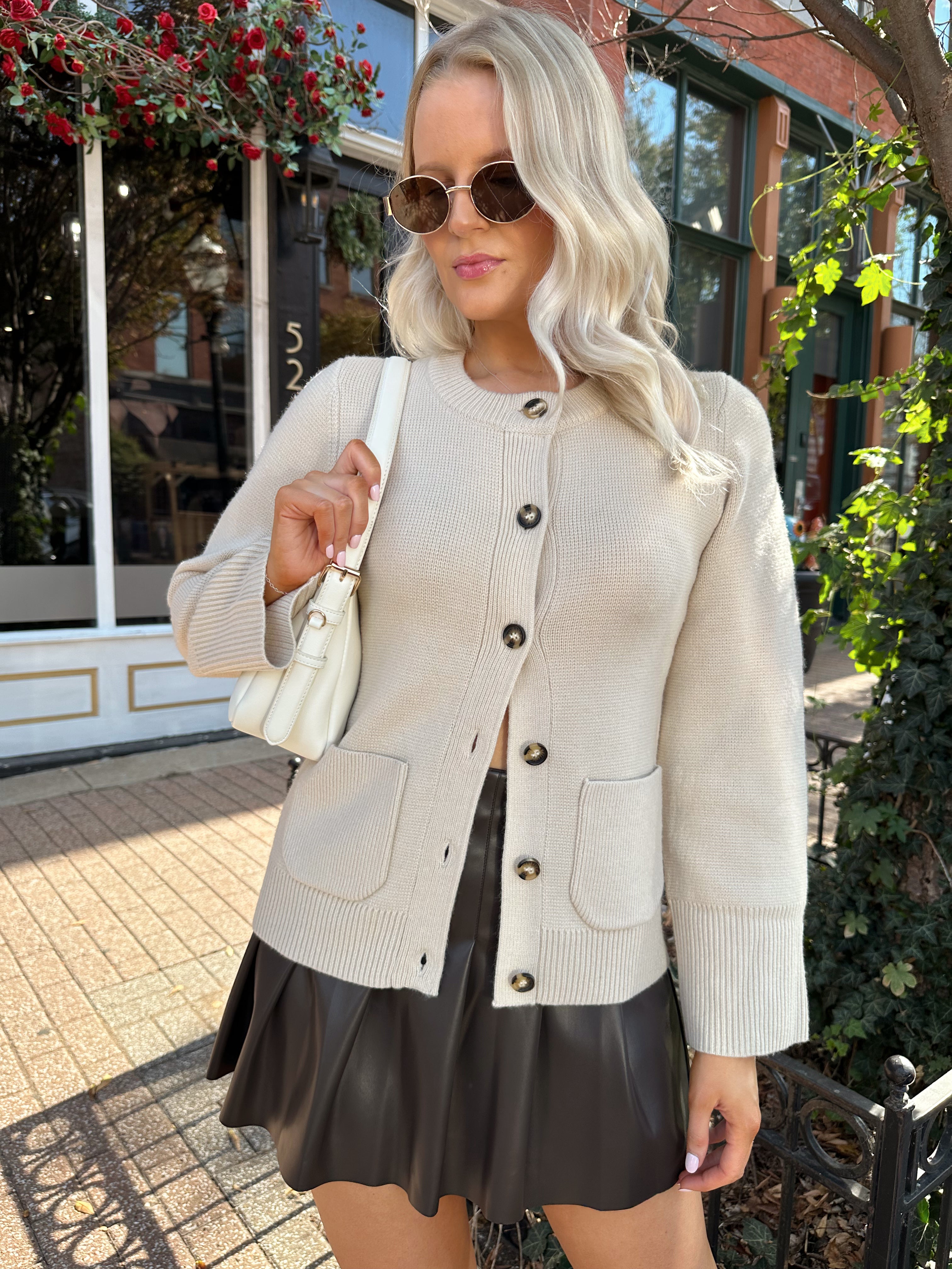 Woman wearing ecru button up fitted cardigan with brown leather mini skirt. 