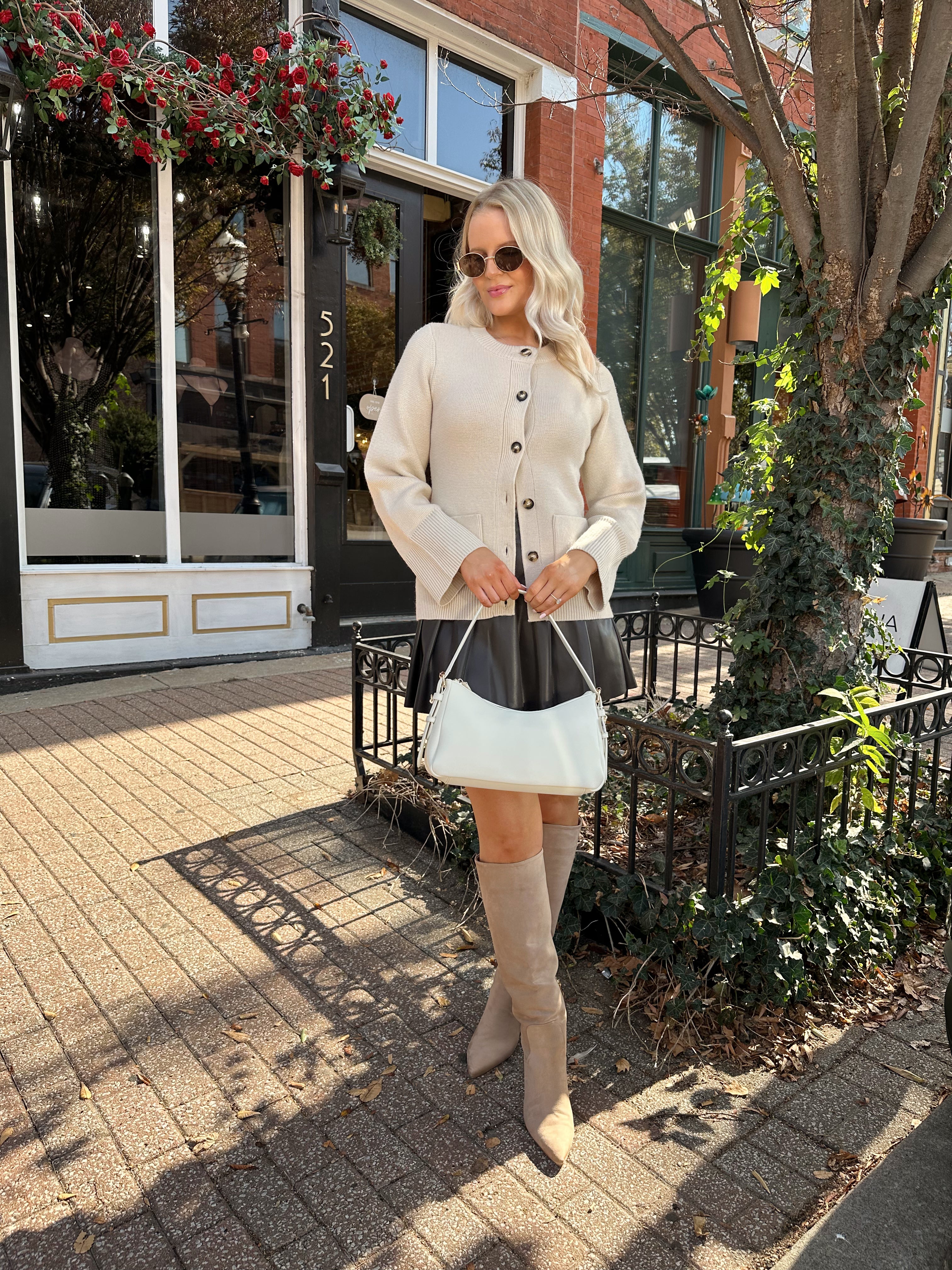 Woman wearing ecru button up fitted cardigan with brown leather mini skirt. 