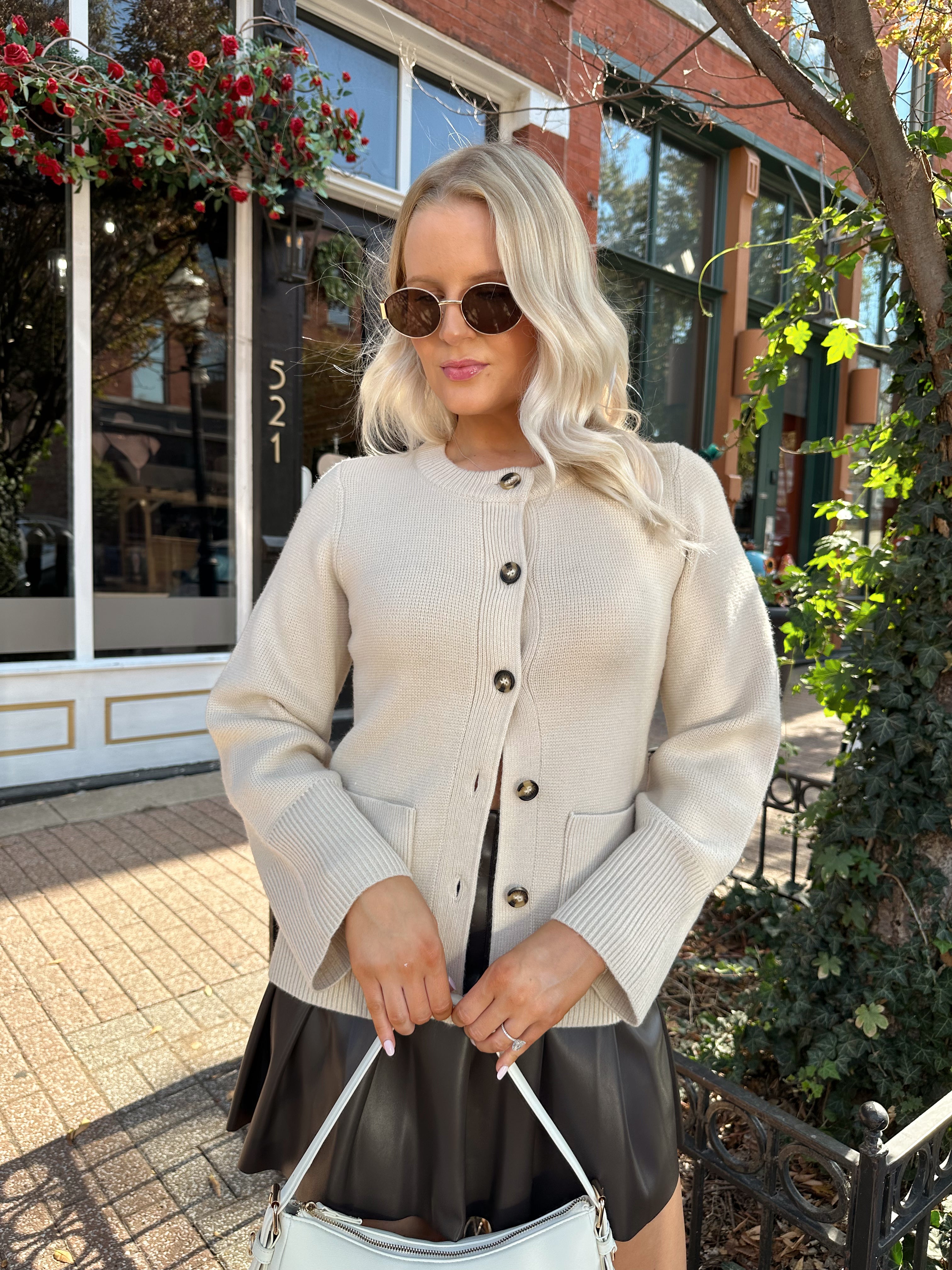 Woman wearing ecru button up fitted cardigan with brown leather mini skirt. 