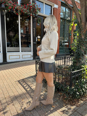 Woman wearing ecru button up fitted cardigan with brown leather mini skirt. 