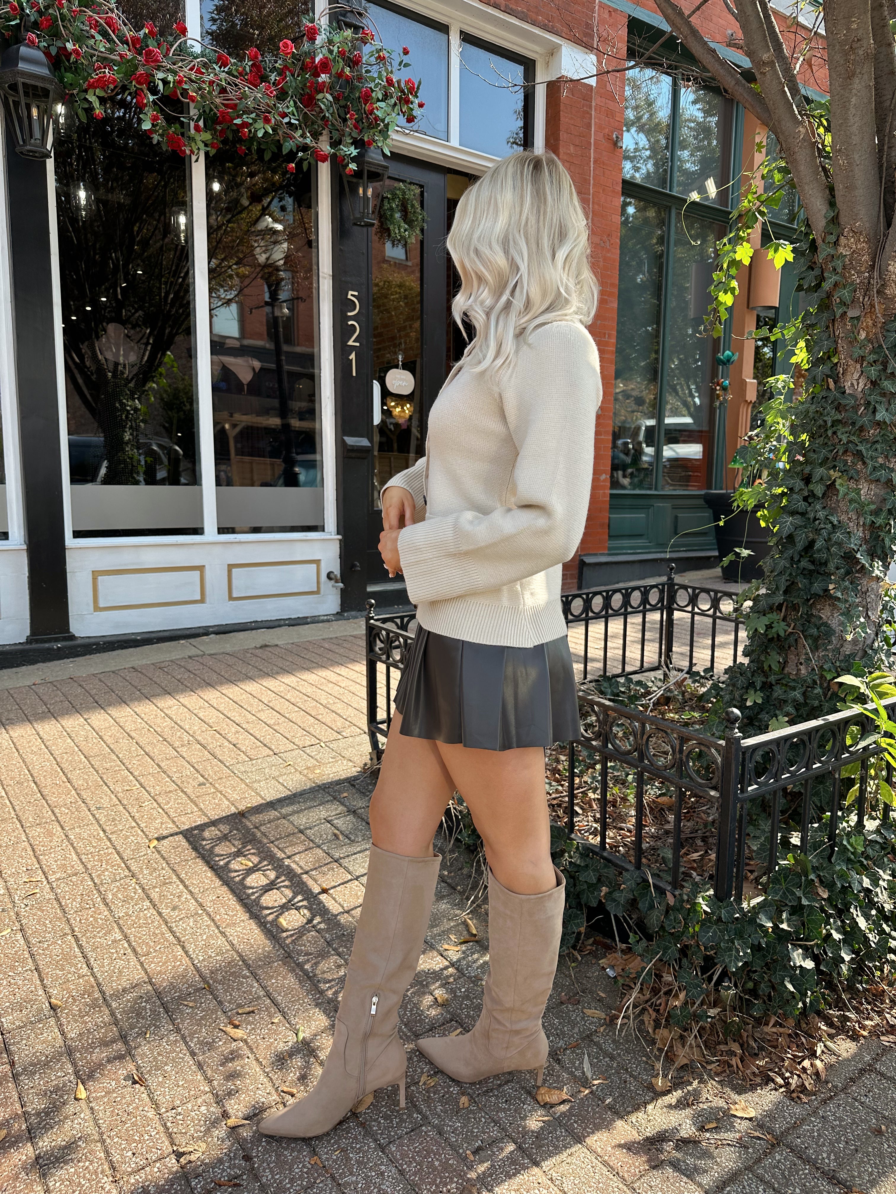 Woman wearing ecru button up fitted cardigan with brown leather mini skirt. 