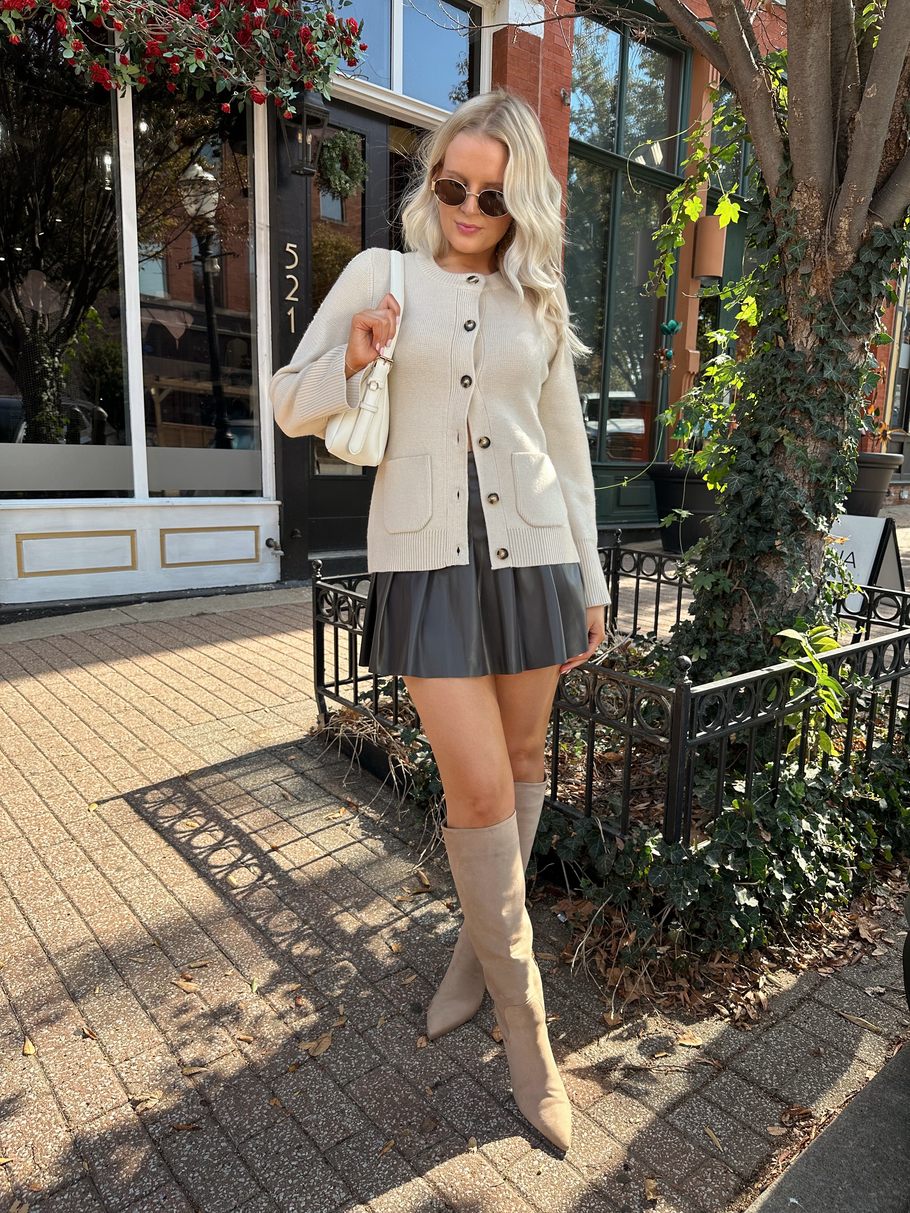 Woman wearing ecru button up fitted cardigan with brown leather mini skirt. 