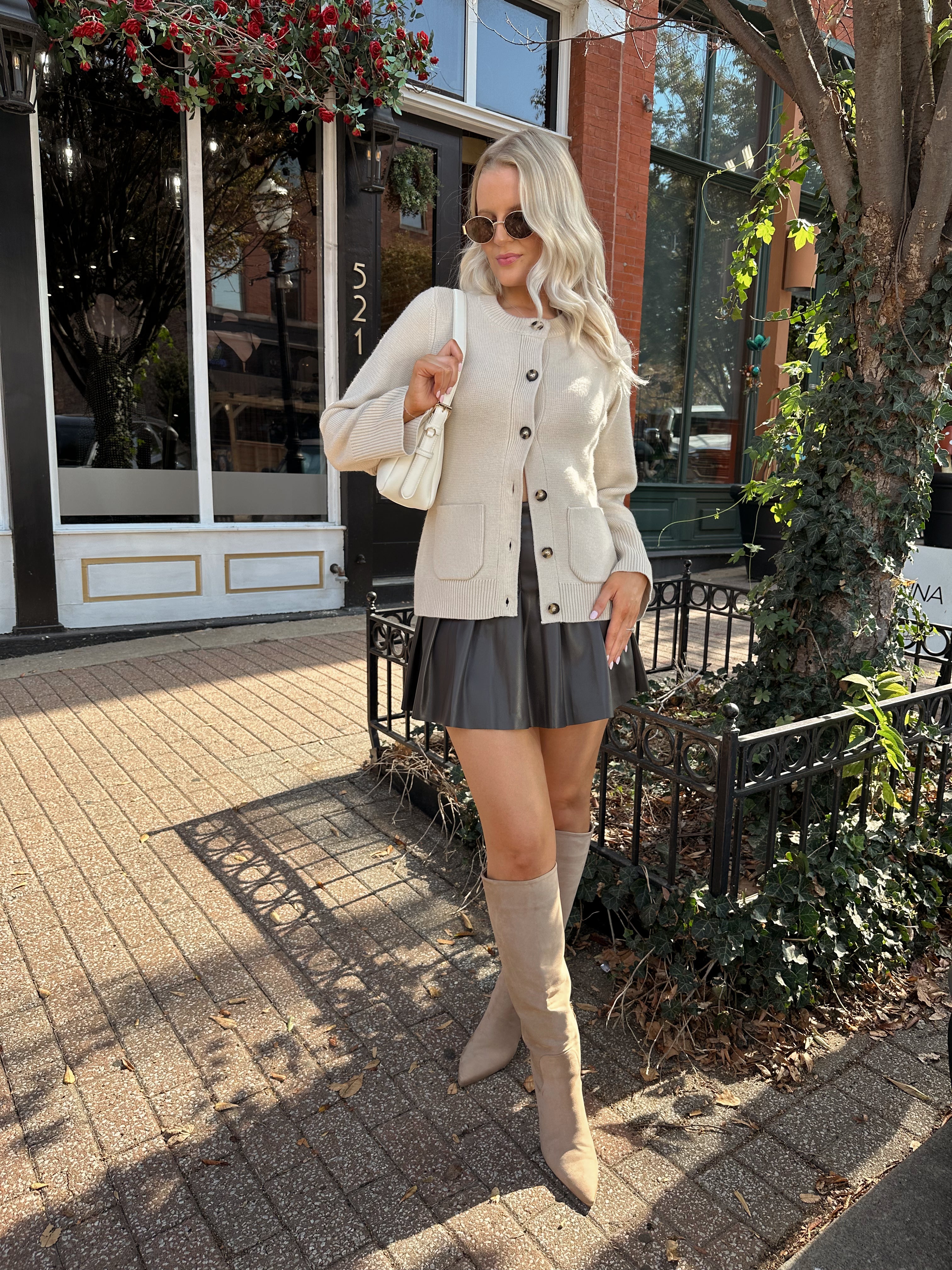 Woman wearing ecru button up fitted cardigan with brown leather mini skirt. 