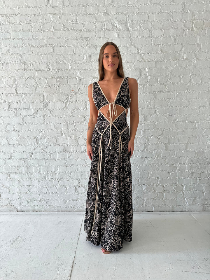Woman wearing beige  and black floral maxi dress with cutout midsection, and cutout sides. 