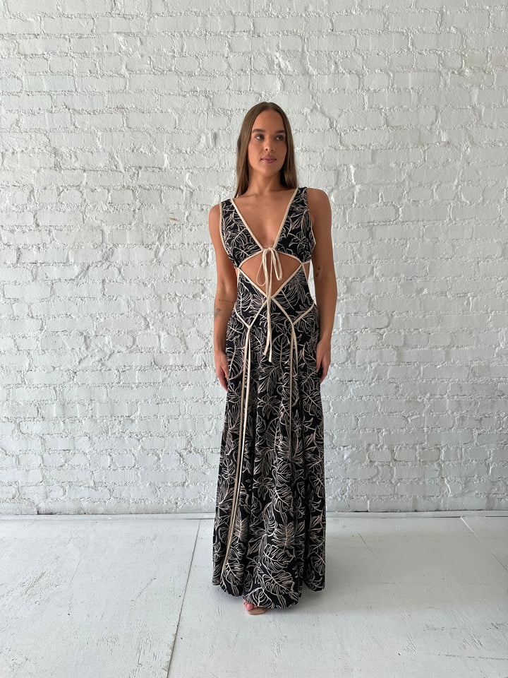 Woman wearing beige  and black floral maxi dress with cutout midsection, and cutout sides. 