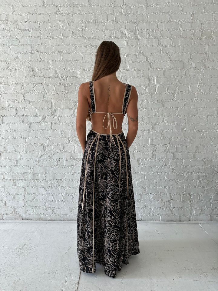 Woman wearing beige  and black floral maxi dress with cutout midsection, and cutout sides. 