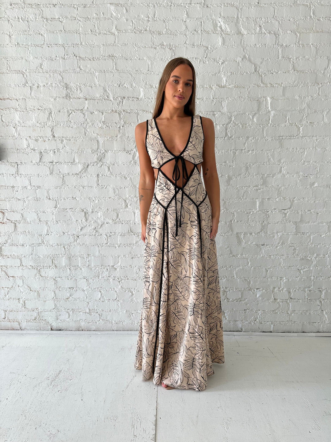 Woman wearing beige floral maxi dress with cutout midsection, and cutout sides. 