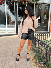 Woman wearing oatmeal colored knit chunky cardigan with gold button closure and functional pockets.
