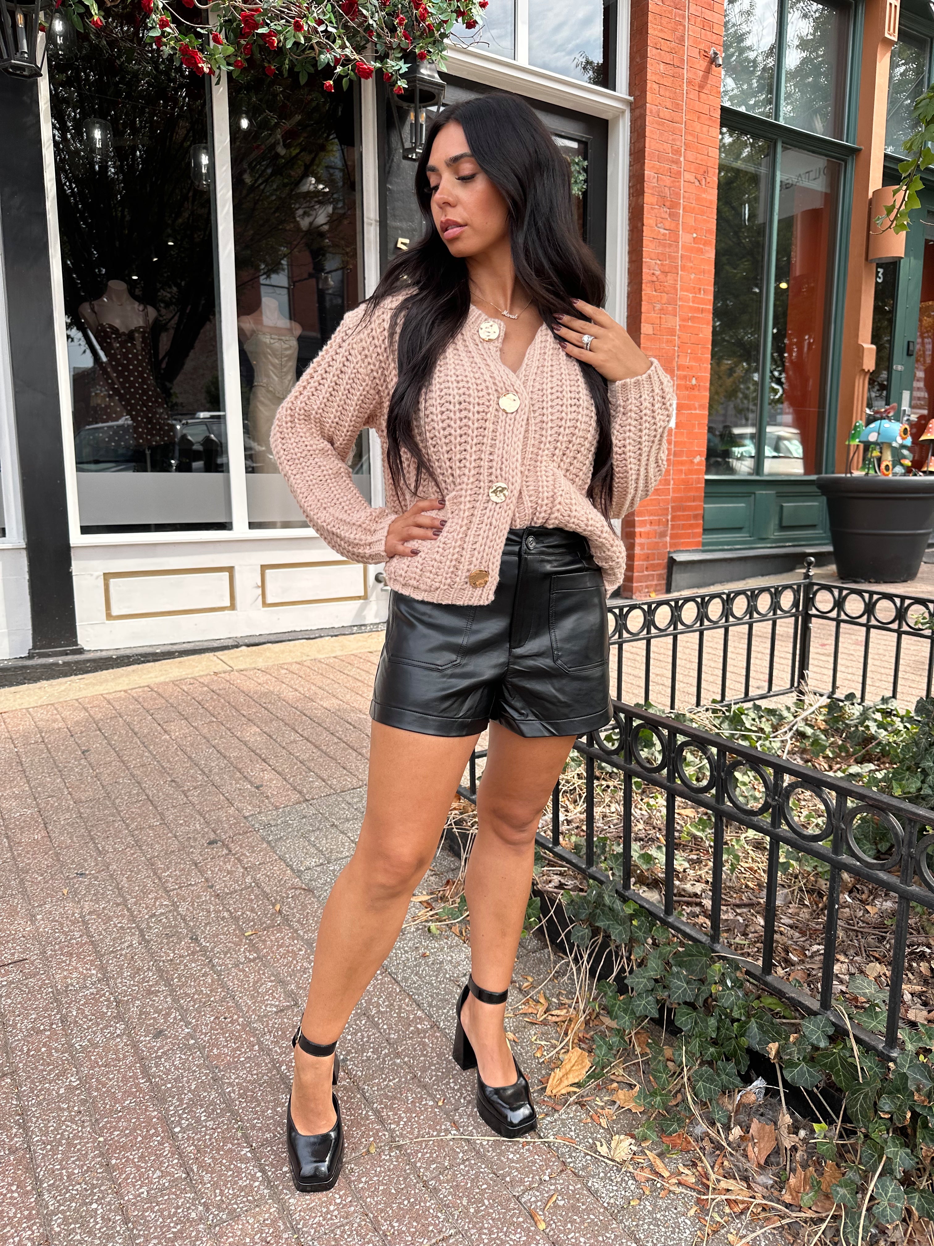 Woman wearing oatmeal colored knit chunky cardigan with gold button closure and functional pockets.