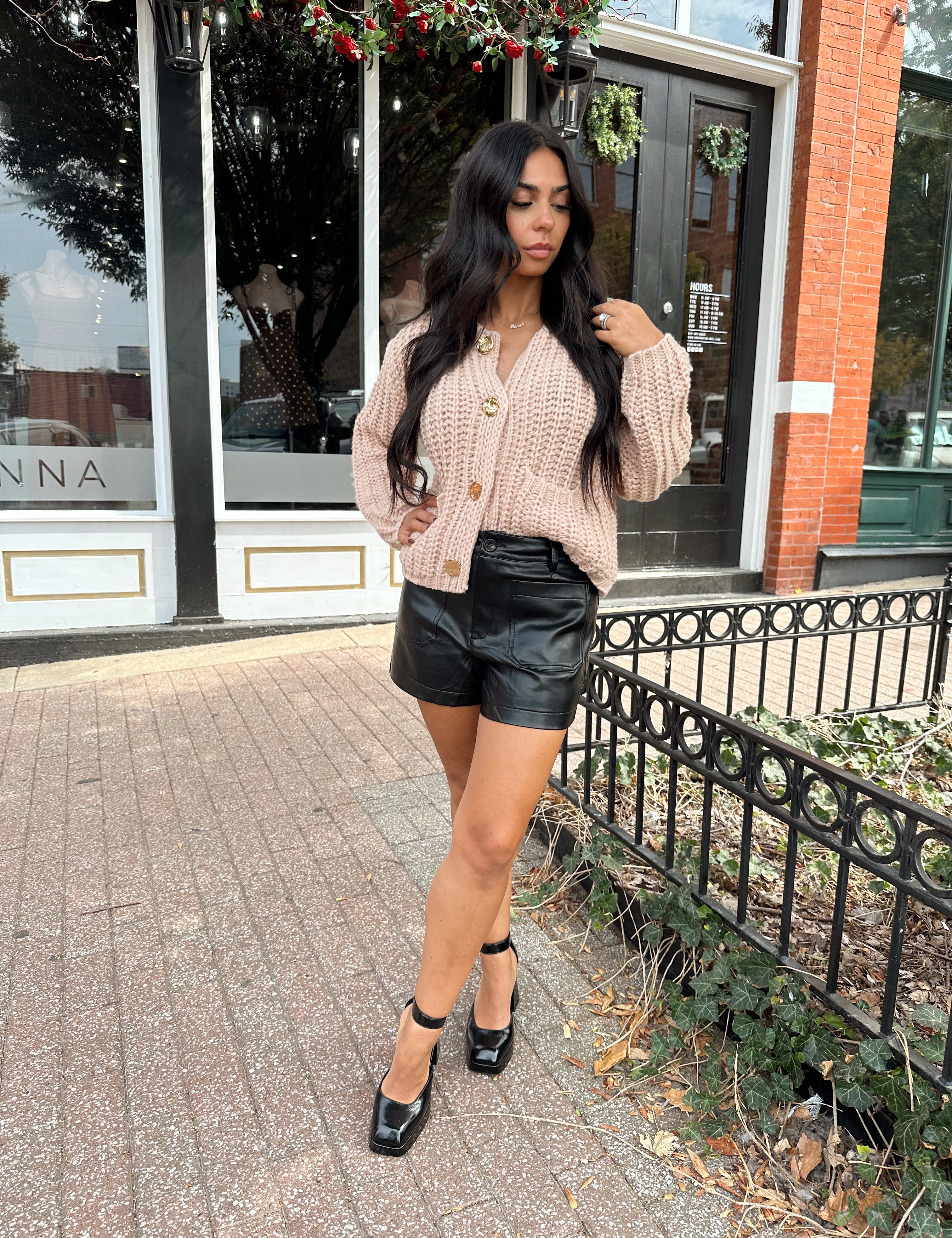 Woman wearing oatmeal colored knit chunky cardigan with gold button closure and functional pockets.