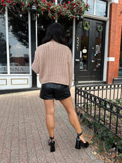 Woman wearing oatmeal colored knit chunky cardigan with gold button closure and functional pockets.