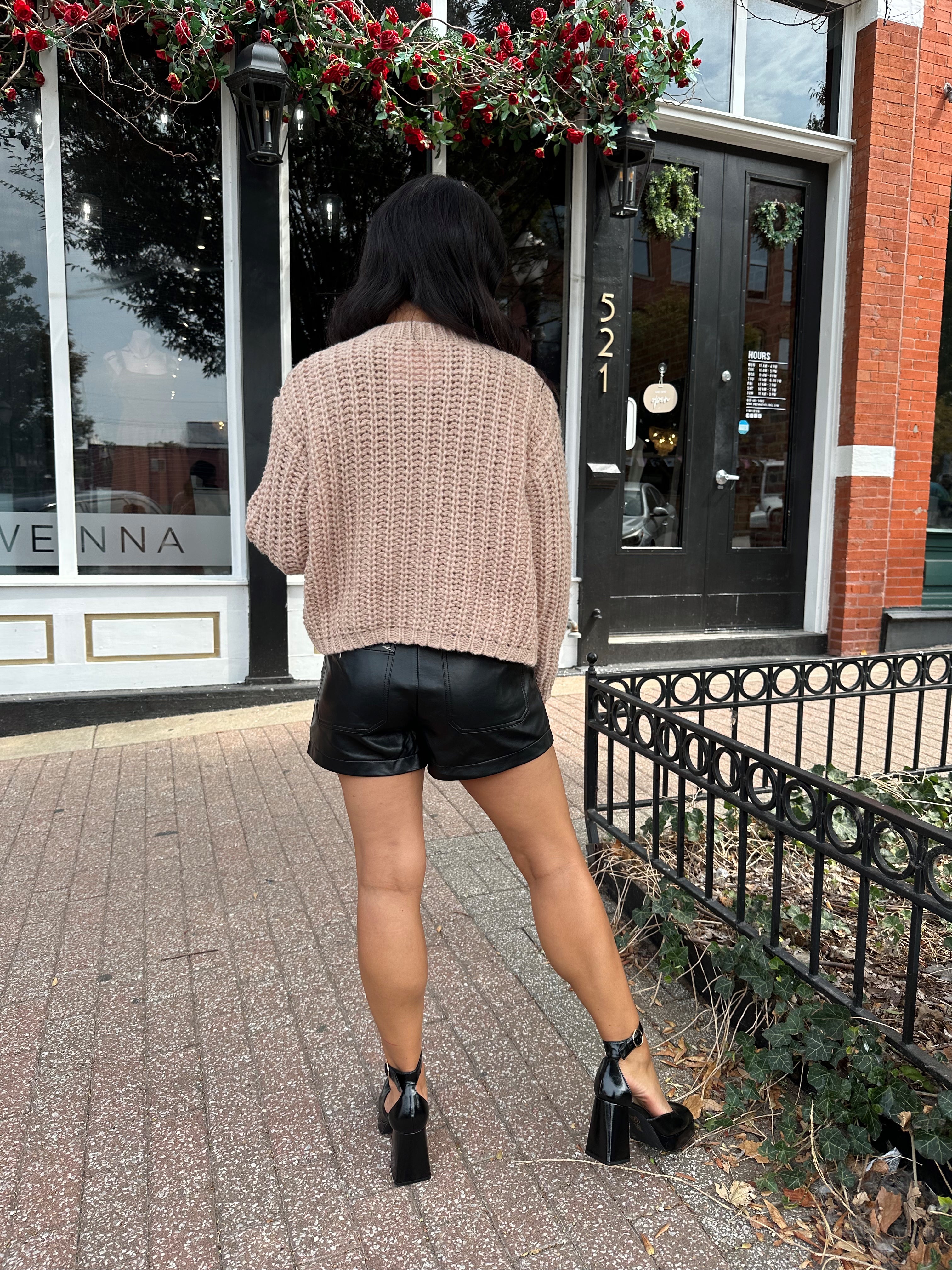 Woman wearing oatmeal colored knit chunky cardigan with gold button closure and functional pockets.