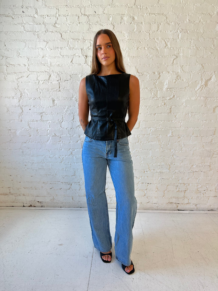 Woman wearing black leather top with belted waist detail.