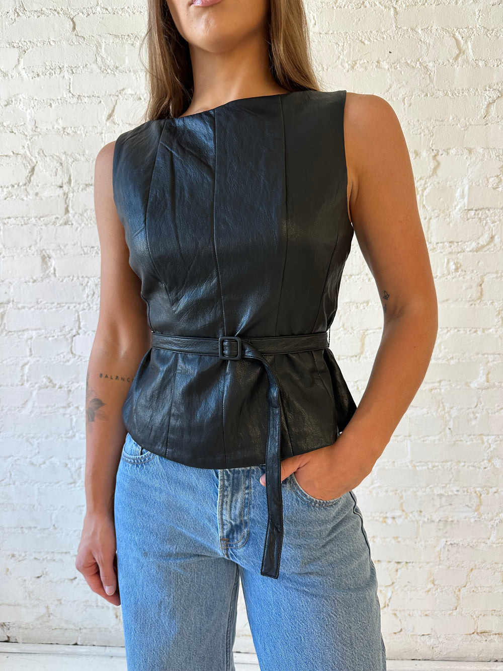 Woman wearing black leather top with belted waist detail.