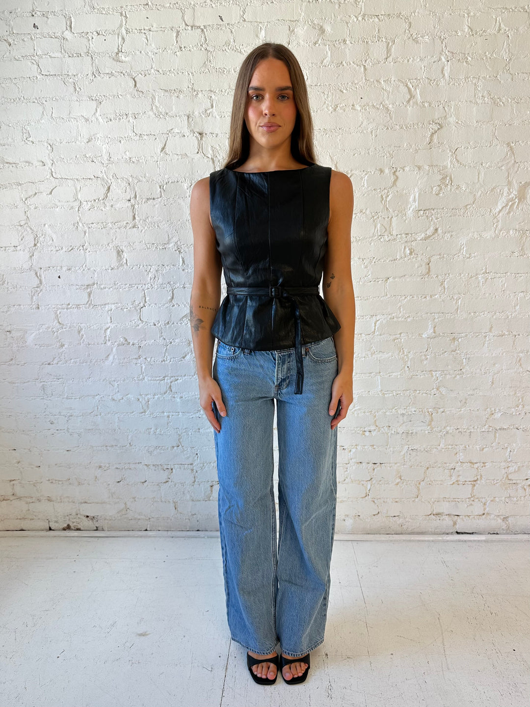 Woman wearing black leather top with belted waist detail.