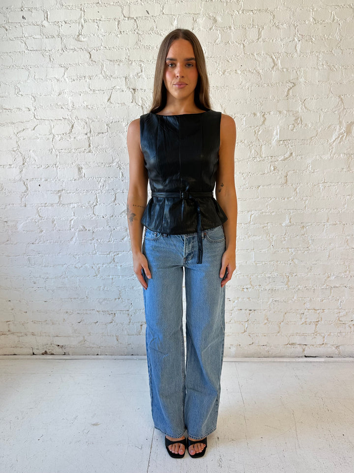Woman wearing black leather top with belted waist detail.