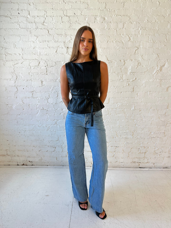 Woman wearing black leather top with belted waist detail.