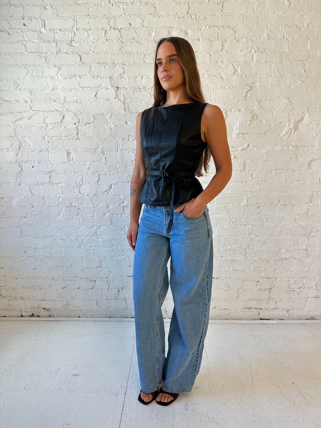 Woman wearing black leather top with belted waist detail.
