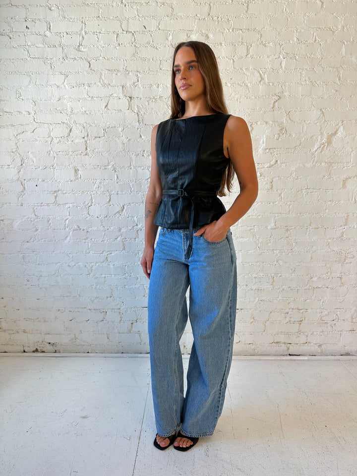 Woman wearing black leather top with belted waist detail.