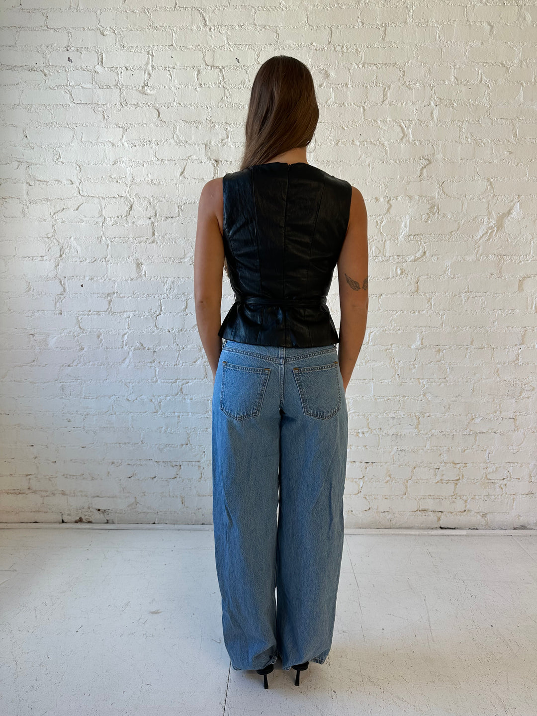 Woman wearing black leather top with belted waist detail.